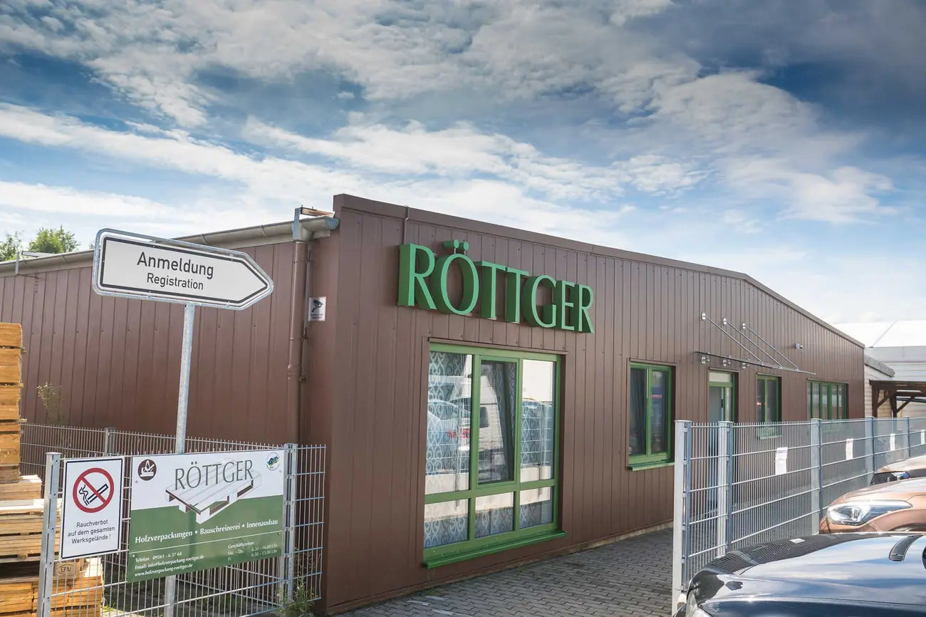 Firmengebäude der Holzverpackung Röttger mit grünem Schriftzug, davor ein Wegweiser mit der Aufschrift Anmeldung